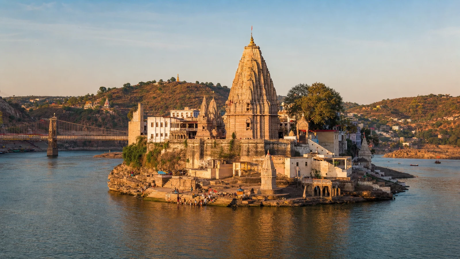 मध्य प्रदेश में नर्मदा नदी के मांधाता द्वीप पर स्थित ओंकारेश्वर ज्योतिर्लिंग मंदिर, घाटों, पहाड़ियों और पुल के साथ।